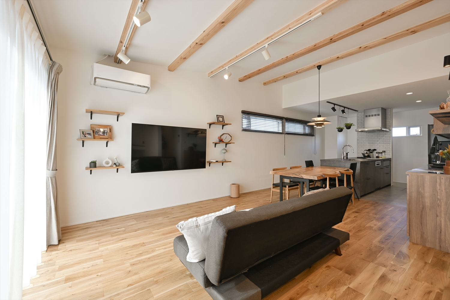 大きな窓から光が差し込む平屋のリビング、壁掛けテレビとシェルフ収納のあるR+house注文住宅