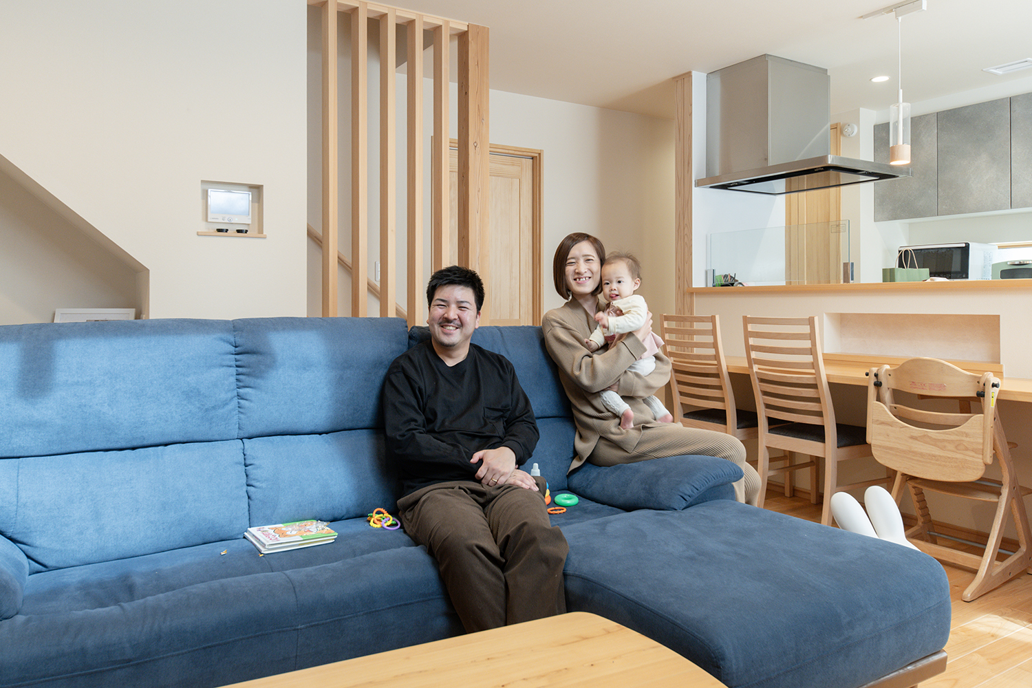 青いソファとカウンターキッチンがあるリビングで過ごす家族／全館空調で快適な注文住宅