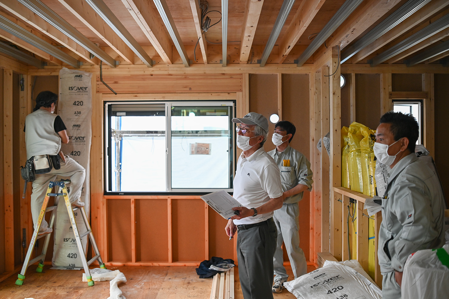 実棟でのグラスウール充填断熱講習。施工管理者と大工が欠損ゼロの充填・気流止め・耳の留め付けを確認する様子