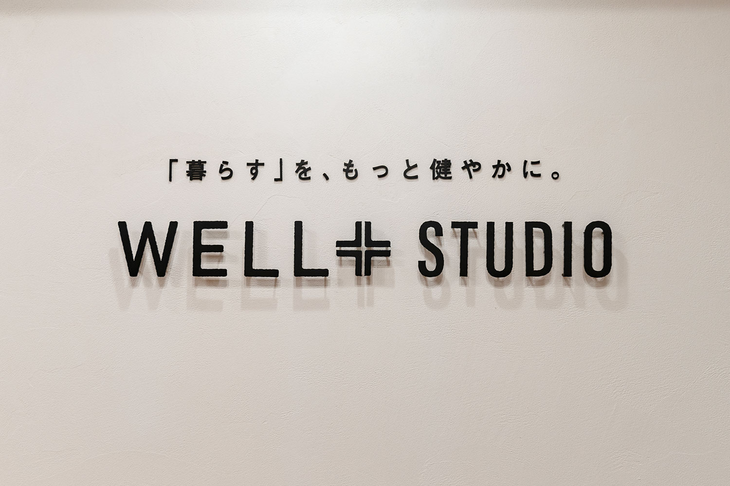 「暮らすを、もっと健やかに。」のメッセージとWELL+STUDIOロゴサインが飾られたエントランスのオーナメント