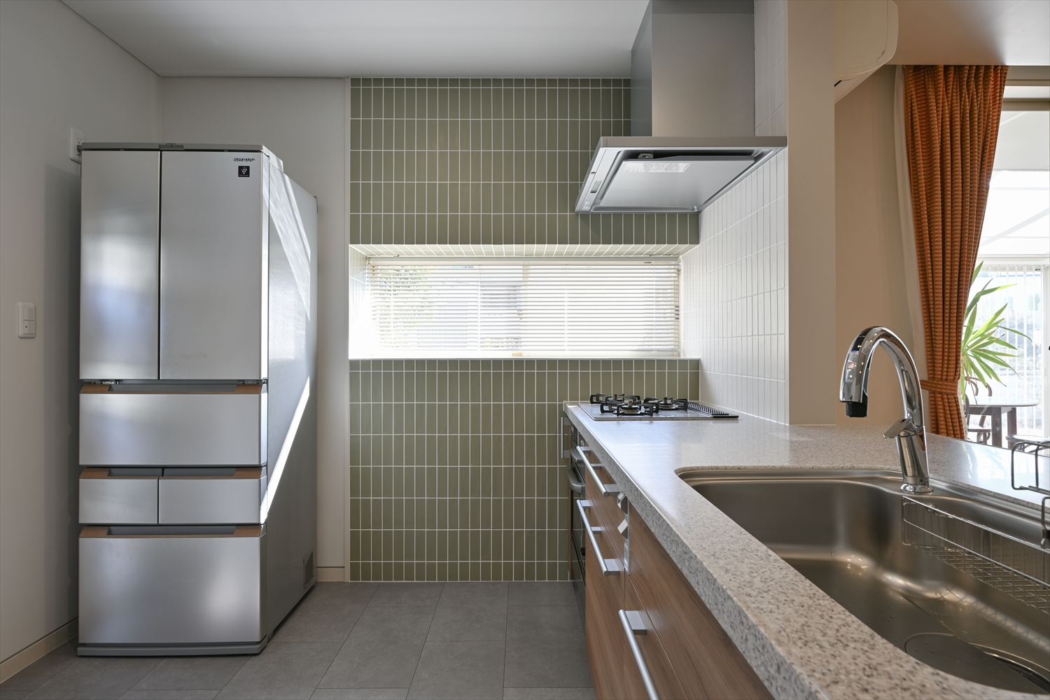グリーンの縦長タイルと窓が映えるキッチン（リフォーム後）
