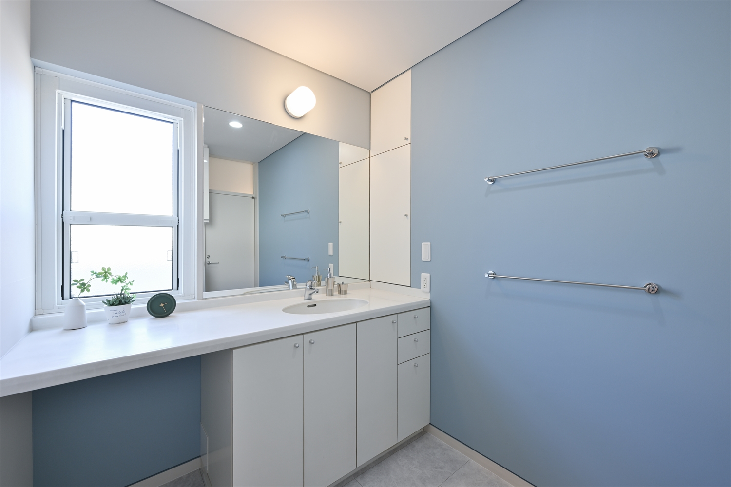 ブルーグレーの壁と白い洗面台の洗面室（リフォーム後）