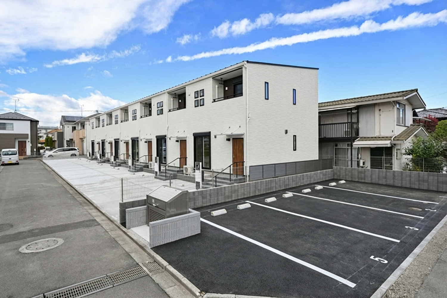 賃貸住宅に隣接する敷地内駐車場、区画ラインと車止めがある舗装スペース