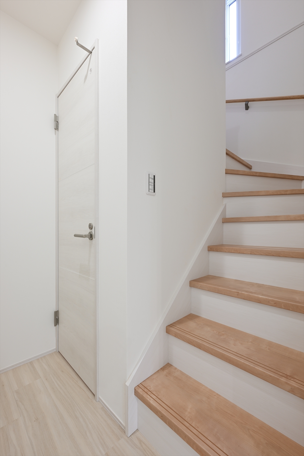 木目の踏板と手すりのある室内階段、採光窓があるホール