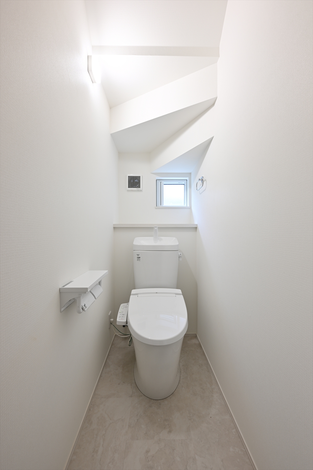 窓付きのトイレ空間、温水洗浄便座と背面カウンターがある