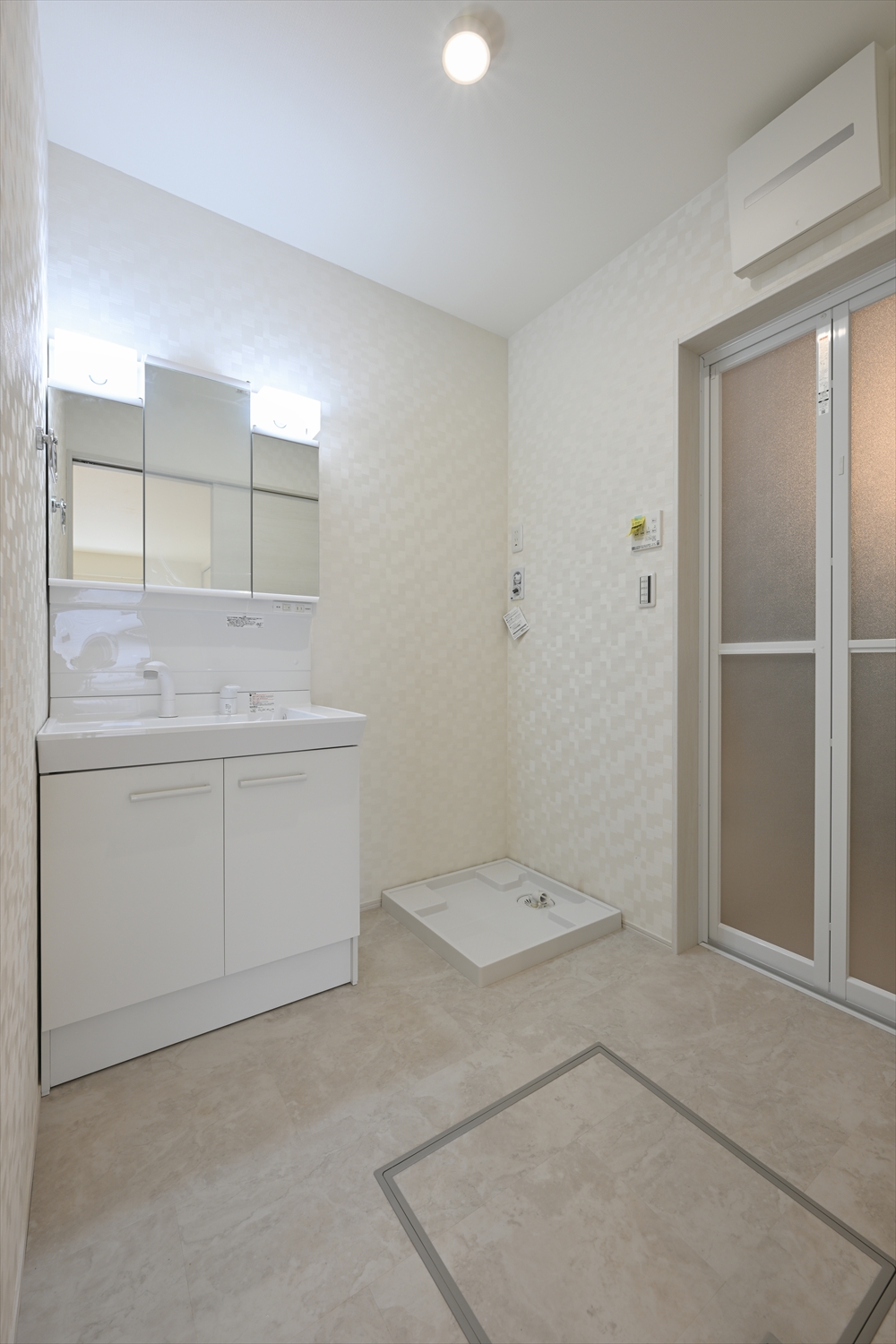 三面鏡付き洗面化粧台と洗濯機パンがある洗面脱衣室、引き戸の出入口