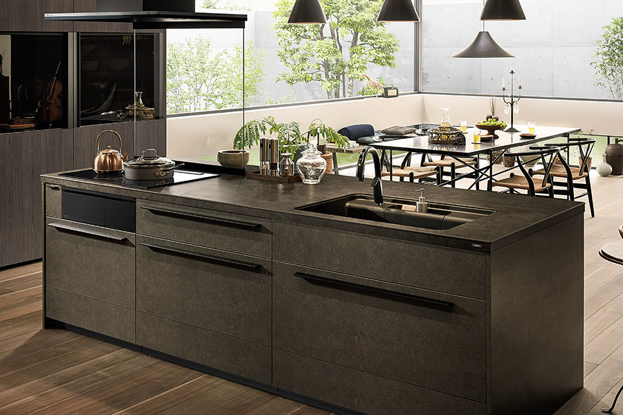 LIXILのシステムキッチン「リシェル」の施工イメージ。ダークカラーのアイランドキッチンで、ミニマルな空間に整うキッチンリフォーム