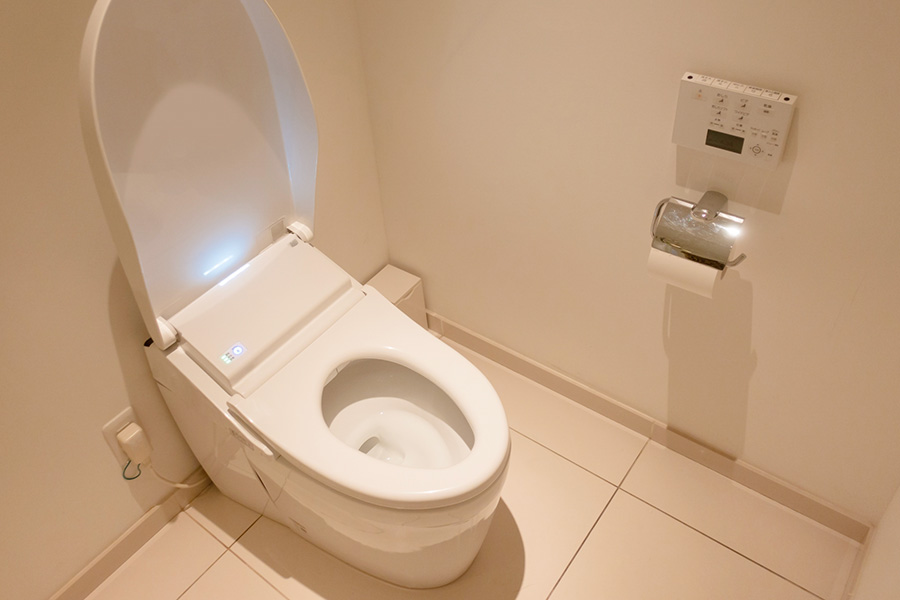 便座が開いたトイレと壁付けリモコンがあるトイレ空間