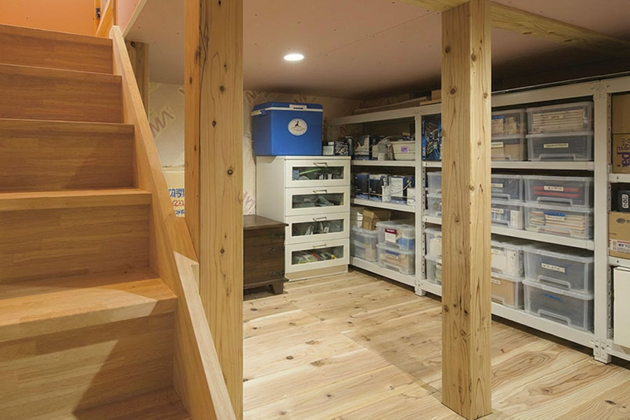 階段下からつながる半地下収納スペース。木の床と棚を備え、日用品や季節物を整理しやすい半地下空間