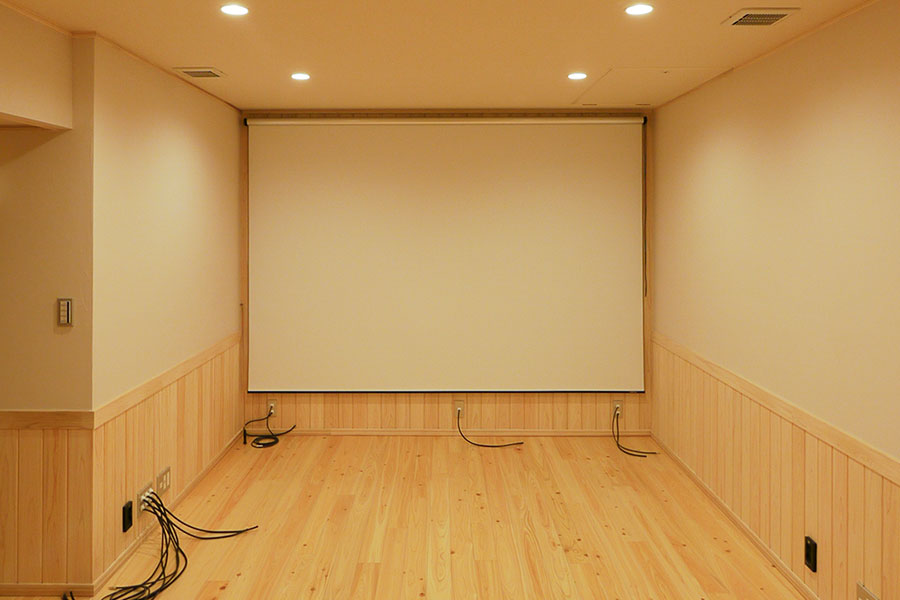 半地下のシアタールーム空間。木の床と腰壁で仕上げた空間にスクリーンを設置したWELL+の半地下イメージ