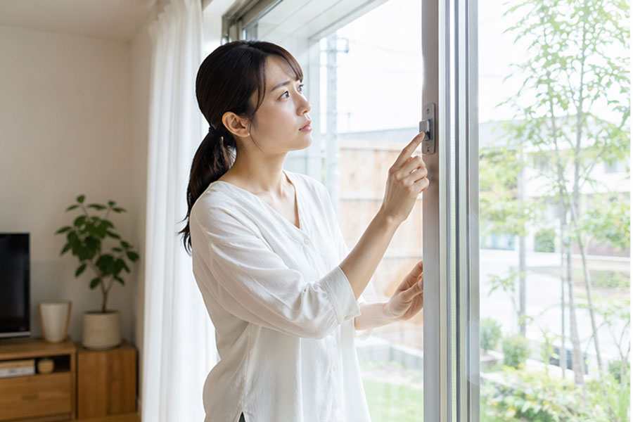 掃き出し窓の鍵まわりを確認する女性