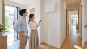 新築注文住宅の玄関ホールで感震ブレーカー付き分電盤を確認する日本人夫婦